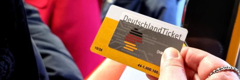 Eine Hand hält ein Deutschlandticket neben einen Stopp-Knopf an der Tür einer Straßenbahn